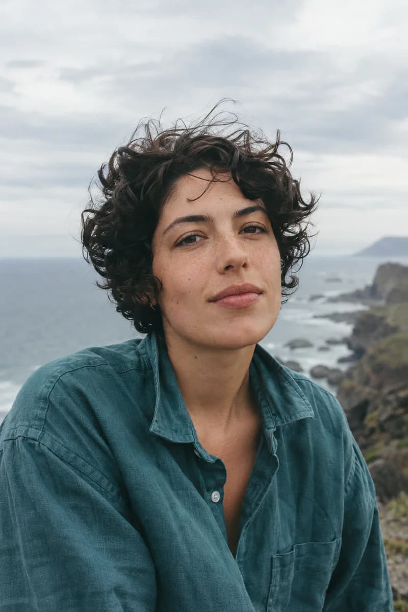 An artist with dark curly hair in the wind on a coastal headland